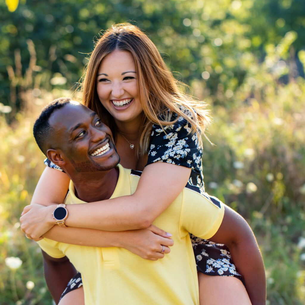 Relationship Reset: Ready. Close up fun portrait of happy multiracial couple doing piggybacking outdoors. Black man carrying caucasian girlfriend on back against green nature background.
